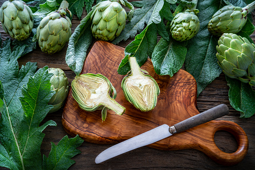 Whole fresh raw artichokes on green background, flat lay