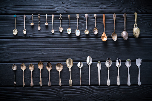 Cutlery home inventory teaspoon  in a row on black wooden background with vintage, wooden colorful stainless steel porcelain and silver
