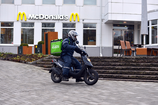 A courier working for Uber food delivery service, riding a scooter in front of a McDonalds restaurant in the city streets of Gothenburg, Sweden
