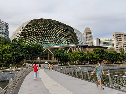 May 2020. Singapore. Scene of everyday Singapore during the world pandemic of 2020 Coronavirus / COVID - 19 people walking with masks one and exercising while a architectural marvel stands in the background (The Esplanade Theater) aka the Durian. Man is seen walking near camera while wearing a mask