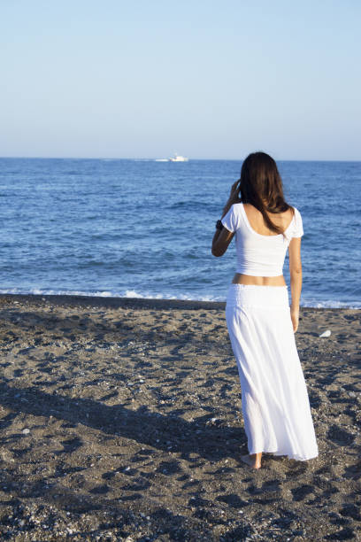 istock Girl dressed in white with her back to the beach. Tranquil scene 1226549866