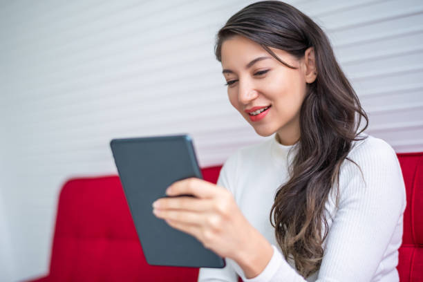 istock Beautiful attractive young Asian woman using smart phone or cellphone or tablet while sitting on red sofa at living room in the morning 1226549944