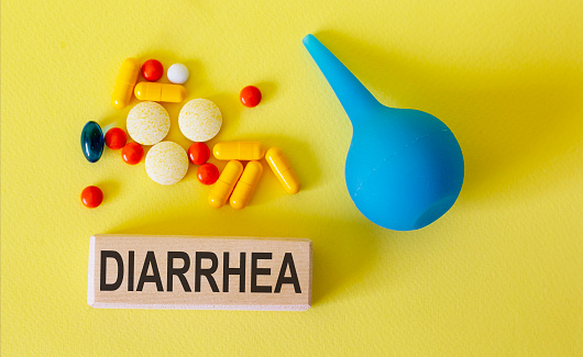 Text diarrhea on a wooden block and enema, pills on a light background