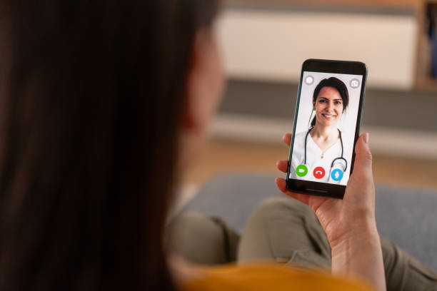 Video call with doctor Woman having video call consulting with family doctor over the shoulder view photos stock pictures, royalty-free photos & images