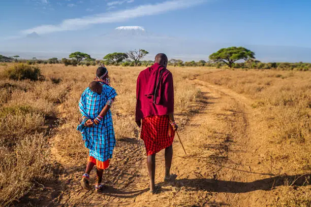 African family from Masai tribe walking on savannah with their baby, Kenya, Africa. Mount Kilimanjaro on the background, central Kenya, Africa. Maasai tribe inhabiting southern Kenya and northern Tanzania, and they are related to the Samburu.