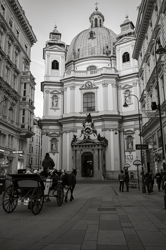 Vienna, Austria - November 1, 2015: Vertical street view of Vienna with Peterskirche or St. Peters Church facade. Ordinary people walk the street. Black and white stylized photo