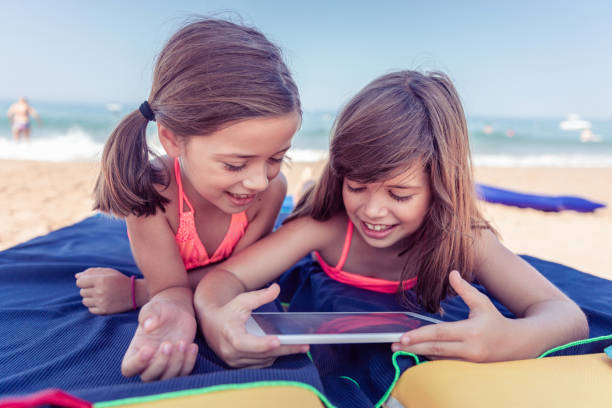 симпатичные девушки загорать и с помощью цифрового планшета - child beach digital tablet outdoors стоковые фото и изображения