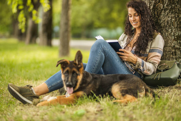 Young female student reading a book and lying down near her dog at the park