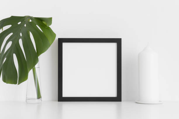 istock Black square frame mockup with a monstera leaf in a glass vase and a candle  on a white table. 1226575515