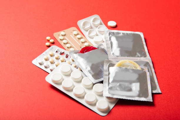 빨간 배경��에 피임약 과 콘돔. 클로즈업 - condom aids sex education contraceptive 뉴스 사진 이미지