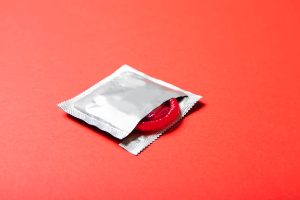 condom coloré sur un fond rouge. médecine et soins de santé - condom photos et images de collection