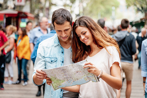 Attractive spanish Tourist Couple looking into Barcelona City Map on the famous Ramblas Street in Barcelona searching for the direction to their next stop. Tourist Couple Lifestyle Barcelona, Catalonia, Spain, Europe