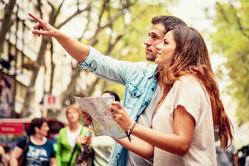 Attractive Tourist Couple on the famous Ramblas Street in Barcelona searching with city map for the direction to their next stop. Man pointing with his finger towards an attraction. Tourist Couple Lifestyle Barcelona, Catalonia, Spain, Europe