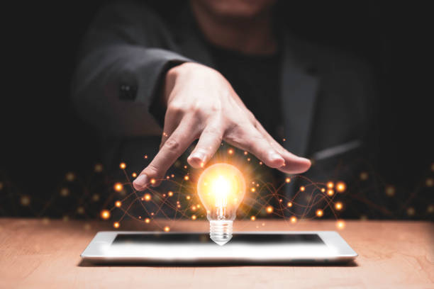istock Businessman hand cover on lightbulb glowing with orange light on tablet. Creating and idea concept. 1226587066