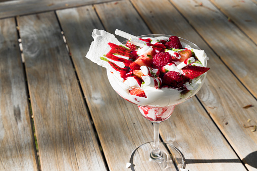 Traditional summer dessert Eton mess. Mixture of meringue, whipped cream, fresh strawberries and raspberries, decorated with mint sauce on wooden table background.