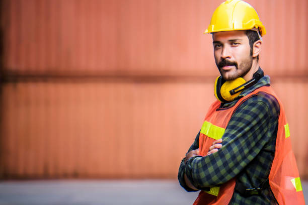 istock Confident Caucasian man engineer wearing yellow safety helmet and check for control loading containers box from Cargo freight ship for import and export, shipping logistic transport concept. 1226589248