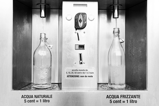 Cheap purified water dispenser for natural water and sparkling water - glass bottles filling with water - Plastic free and environmental sustainability concept - Reuse glass bottles for drinking water