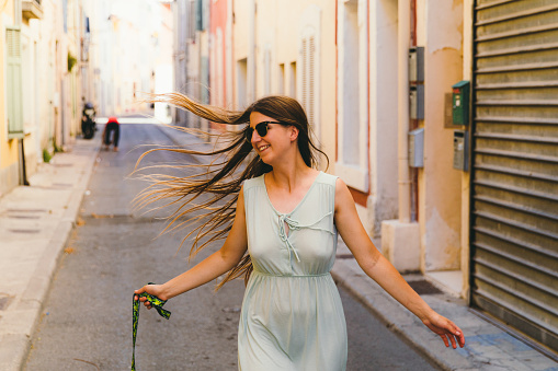 Woman tourist with long hair, in dress exploring the beautiful old town at the coast of French Riviera during bright sunny warm day