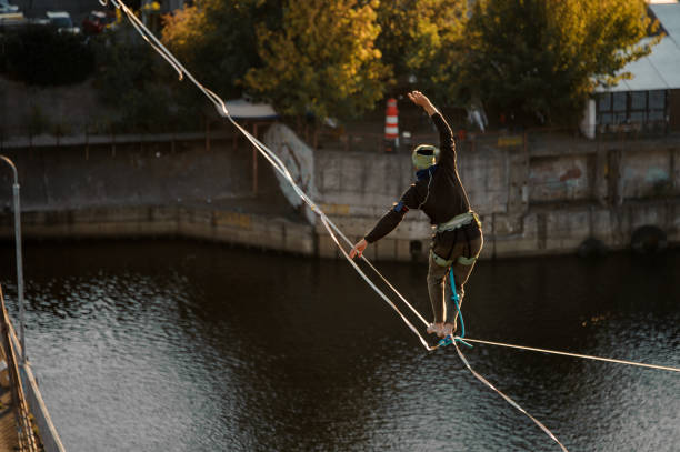 one person walk and balanced on stretched sling. Water and bank of river in background.