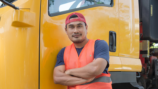 An Asian man was smiling happily beside the yellow truck. He has a career as a transport driver. The transportation business never stops. It must be driven and traveled all the time.