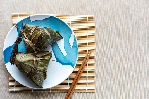 Zongzi is a traditional Chinese food made of glutinous rice stuffed with different fillings and wrapped in bamboo, served on dinning table, close up, copy space, top view, flat lay