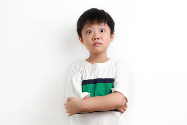 Portraits of young Asian boy arms crossed, looks surprised with big eyes open against a white background.