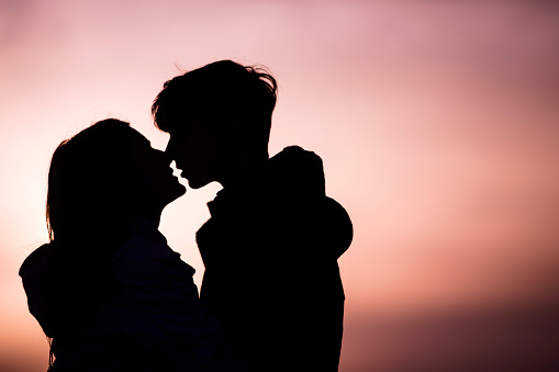Silhouette of Teenage Couple Kissing at Sunset.