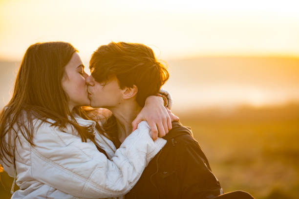 Back Lit Teenage Couple Kissing Outdoors at Sunset stock photo