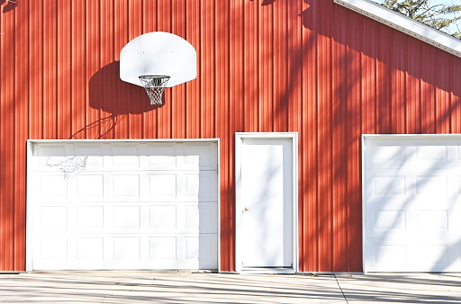 White basketball backboard on red barn or garage with three doors.