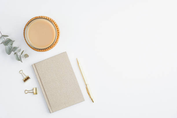 istock Flat lay paper notebook, cup of coffee, eucalyptus leaf and golden accessories on white table. Cozy home office desk, modern feminine workspace top view. Minimalism concept. 1226614983