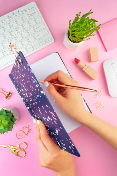 istock Woman's hands with white manicure writes in a blue notebook. Work place on pink background. Flat lay style 1226623823