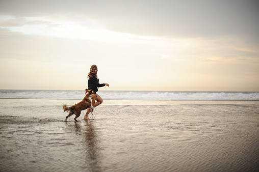 Girl running with her cute dog on the sea coast on the beach in the golden sunset time