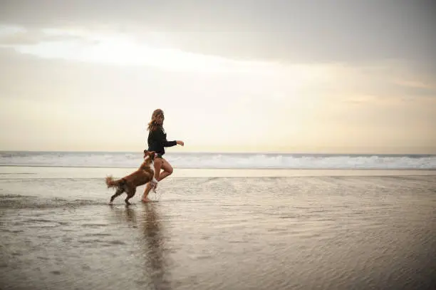 Photo of Girl running with her cute dog on the sea coast