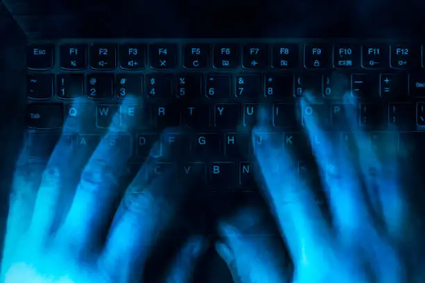 Photo of hands are typing on the keyboard in the dark. The concept of hacking, haters, fake and trolling. Blured