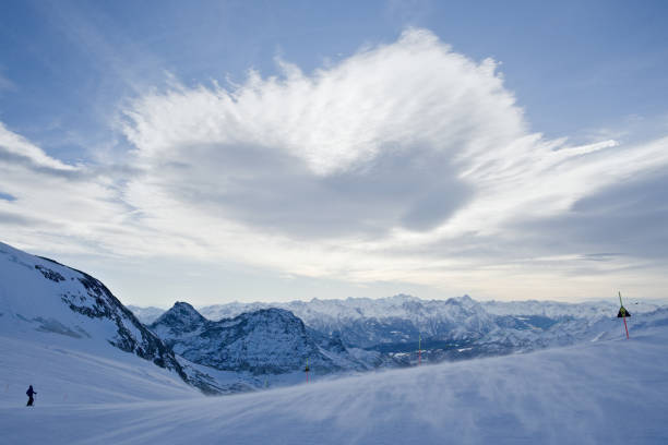 A heart shaped cloud floats over a ski run as part of an expansive mountain vista in the italian alps