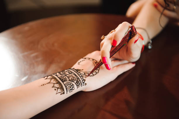 Master mehndi draws henna on a female hand.