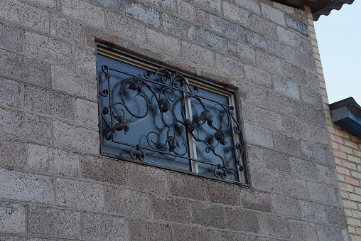 one small window behind a black iron forged lattice on a gray brick wall