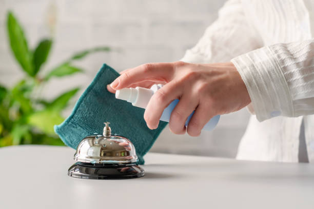 hand of woman cleaning ringing bell on reception desk. disinfection spray, small towel. protection from bacteria and virus. keeping health of guests. hotel service. selective focus - service bell fotos imagens e fotografias de stock