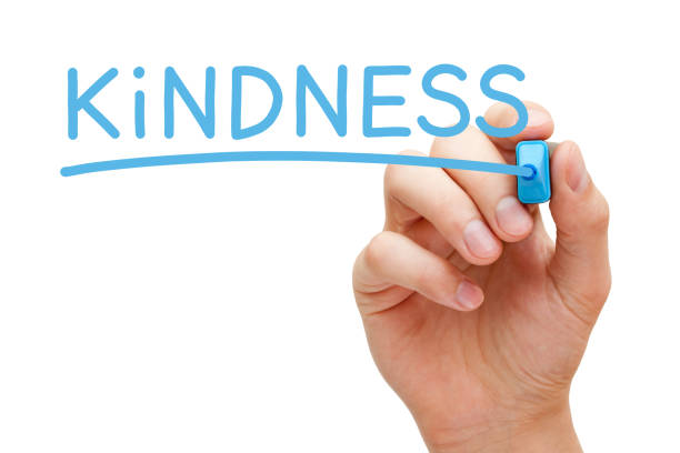 Hand writing the word Kindness with blue marker on transparent wipe board isolated on white background.