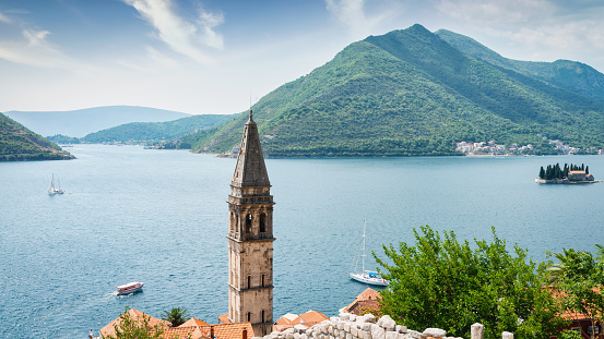 Panorama view over the mediterranean Kotor Bay - Gulf of Kotor surrounded with beautiful Mountains. Old St. Nikola Church Bell Tower of Perast Old Town in the foreground.  The five-story chruch bell tower was built in the year 1691. Perast Town, Bay of Kotor, Kotor, Montenegro, Southeast Europe