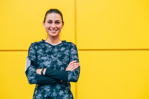 Portrait of a beautiful smiling young sportswoman resting in front of yellow wall.