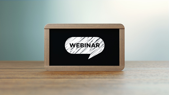 Wooden framed blackboard with webinar icon sitting over wooden surface in front of defocused background. Horizontal composition with copy space. Webinar concept.