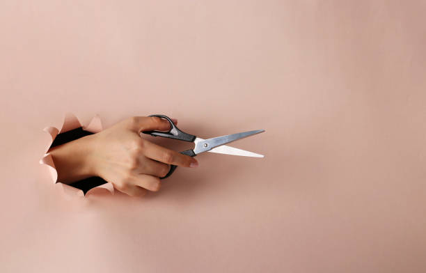 istock Female hand holding scissors through round hole in pink paper, Copy space 1226656695