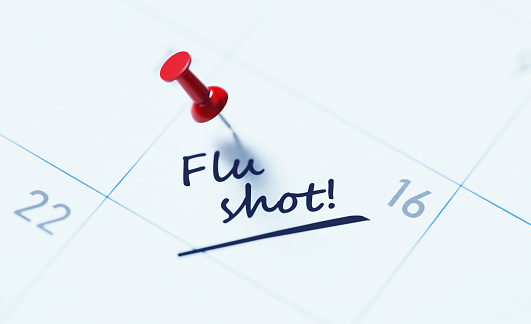 White calendar with red push pin to remind an important date. Flu shot written on the calendar. Calendar and reminder concept. Horizontal composition with copy space.