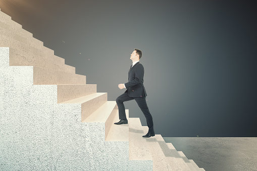 Side view of young businessman climbing on abstract stairs. Career development and job concept