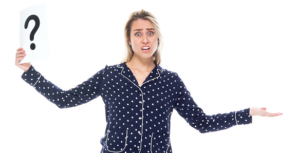 Front view of aged 20-29 years old who is beautiful with blond hair caucasian female standing in front of white background wearing nightwear who is confused and showing question mark