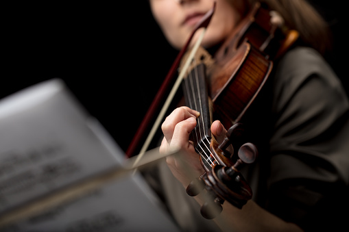 Woman violinist playing a classical baroque violin viewed past a music score on a stand with selective focus to her fingers on the strings