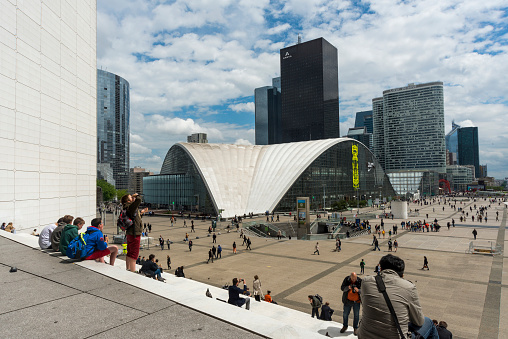 Paris, France - May 23, 2014: People sitting on the white stairs in front of Grande Arche and walking around the square in La Defense, Paris, France.