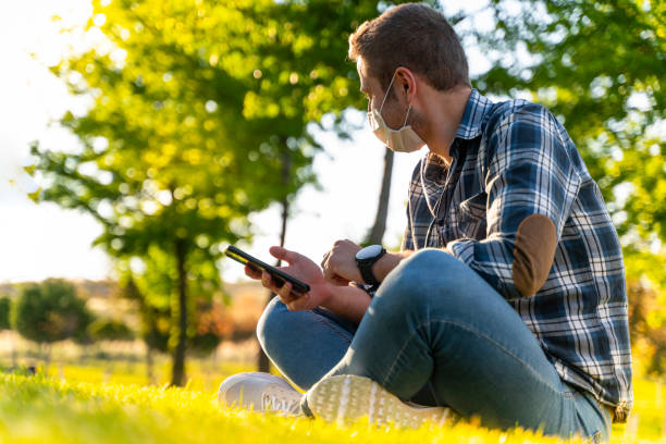 istock young man wearing protective face mask using smart phone in city park 1226666352