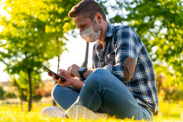 istock young man wearing protective face mask using smart phone in city park 1226668116